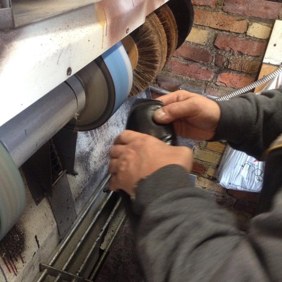 The cobbler's hands polishing a black leather shoe on a buffing wheel